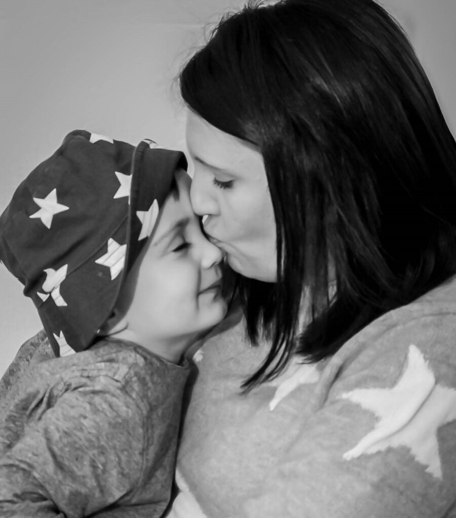 dark haired woman giving affectionate kiss on the nose of a young boy wearing a star-patterned hat