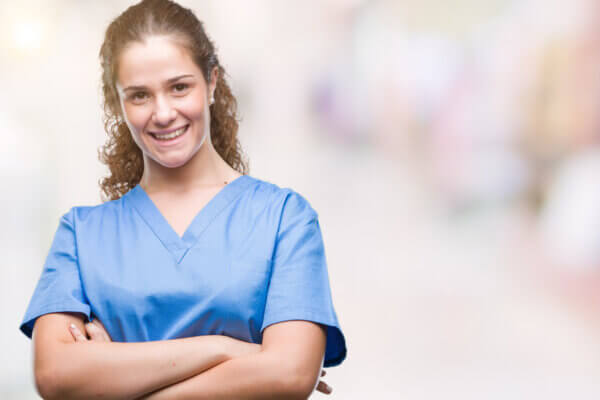 Young woman wearing light blue hospital scrubs with arms folded looking directly at the camera smiling