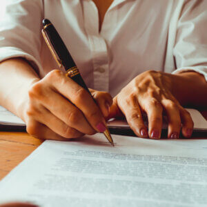 A close up of a womans hands holding pen signing a legal document