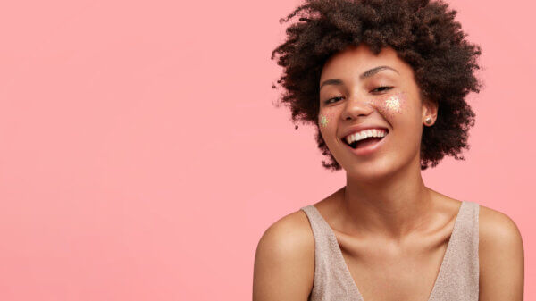 Happy young woman with sparkles and a smile against a pink background