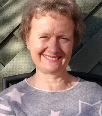 Head and shoulders of woman in a grey sweater with white stars smiling at the camera