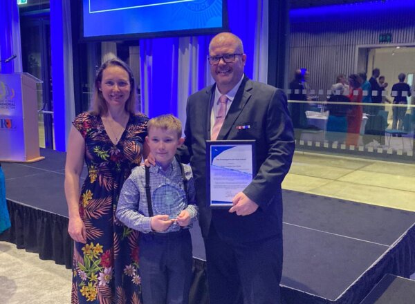 Man holding award certificate, standing alongside partner and son