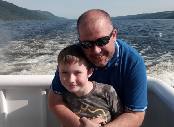 Father affectionately wrapping arms around son, smiling, on a speed boat ride
