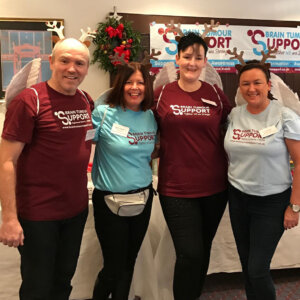 A man and three ladies smiling and wearing charity t-shirts with Christmas decorations behind
