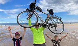 Man holding cycle over his head in celebration of charity bike ride. Two children cheering with arms in the air beside him