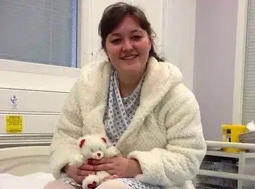Young woman in hospital gown holding a soft toy bear
