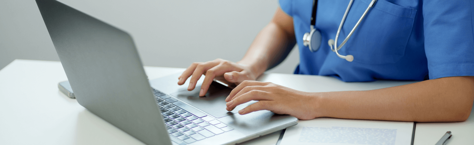 Medical professional in blue scrubs typing on a laptop