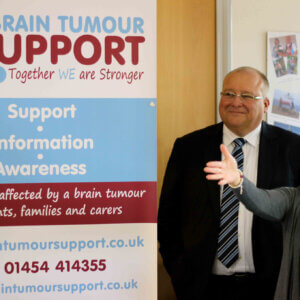 Man in suit and tie standing next to woman pointing towards Brain Tumour Support charity banner