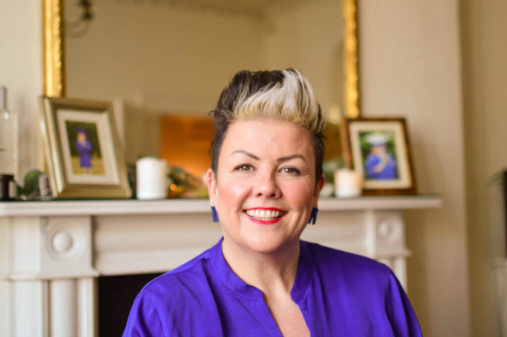 Head and shoulders shot of elegant woman sat in front of a fireplace