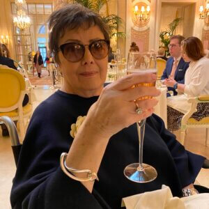 Elderly lady holding up glass of champagne sitting in the Ritz cafe