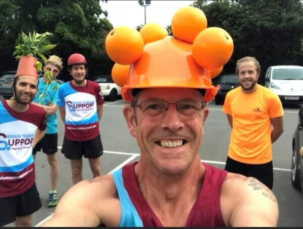 Robin in his bright orange helmet, with Brain Tumour Support colours on his running shirt. Supporters behind him are smiling and also wearing BTS merchandise