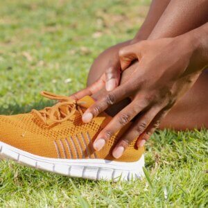 Person wearing a pair of bright yellow and golden coloured trainers. Tying laces on the grass.