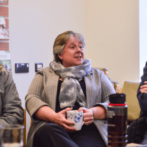 Two men and a woman holding a coffee mug, seated and chatting at a support group