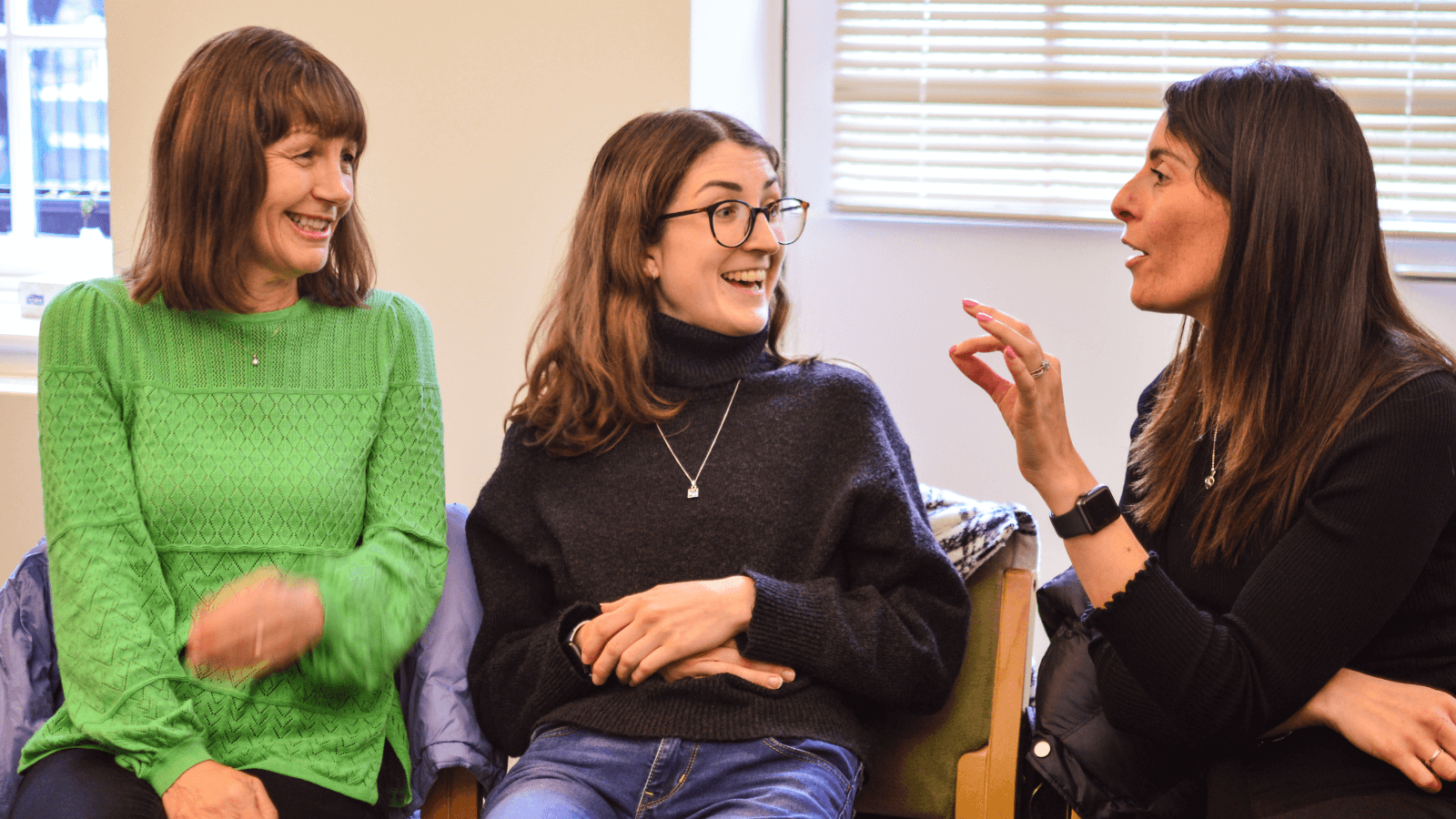 Three women seated, chatting, animated and smiling