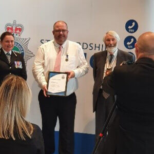 Policeman wearing medal and holding framed certificate