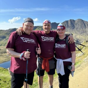 Shaun, group leader Andy, and Shaun's wife Melinda on Snowdon, arms around each other and wearing charity t-shirts