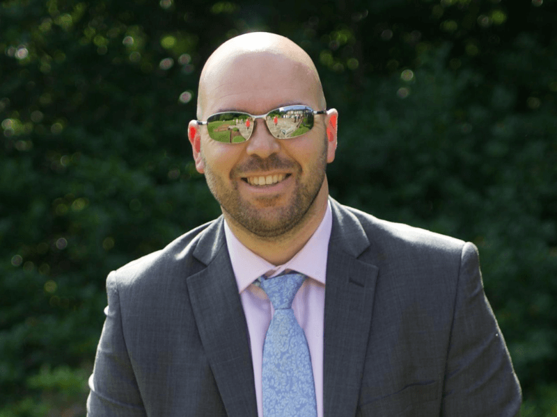 David in suit and tie, wearing sunglasses, smiling