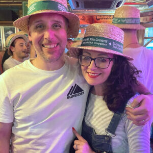 Debbie next to husband Nick, his arm around her shoulder, both wearing straw hats and smiling