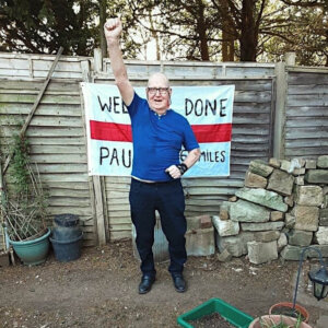 Elderly man standing, smiling and with clenched hand raised triumphantly