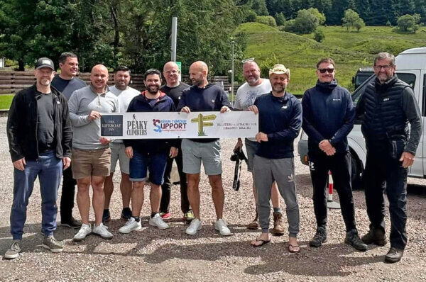 Group of men standing next to a minibus and holding a charity banner for the Three Peaks Challenge