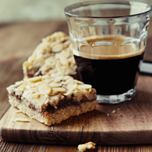 Freshly baked flapjacks on a wooden cake board next to a glass of black coffee