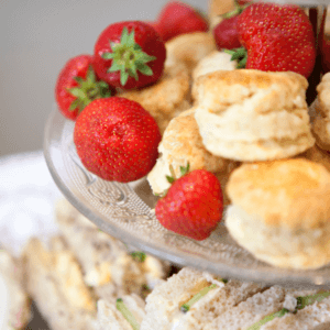 Image shows a glass cake stand filled with freshly baked scones and fresh strawberries