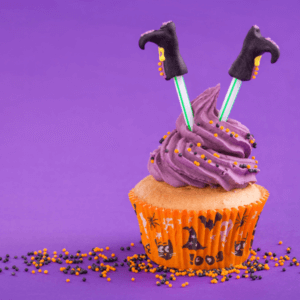 Halloween cupcake set against a purple background with orange and black sprinkles. The cupcakes has witches legs.