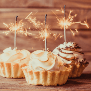 Image shows three cakes with frosting and sparklers on top