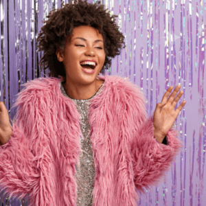 Young woman laughing wearing a pink fluffy jacket and standing against a purple shiny background