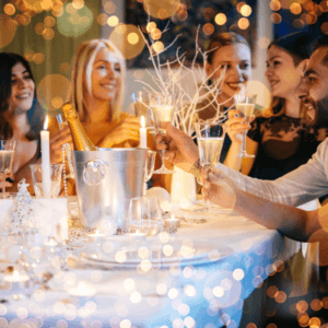 Image shows friends around a dinner table with fairy lights and candles toasting each other