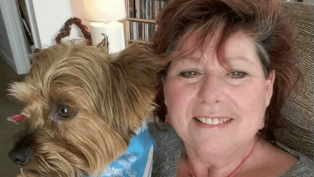 Linda smiling, holding up alongside her a small shaggy terrier dog