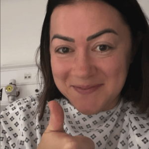 Hannan in hospital smiling and with her thumbs up gesture