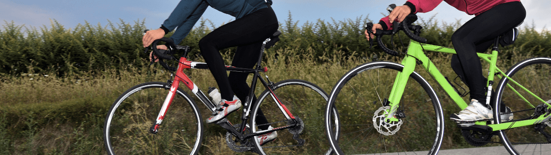 Close up on bikes of two people cycling with hedgerow behind