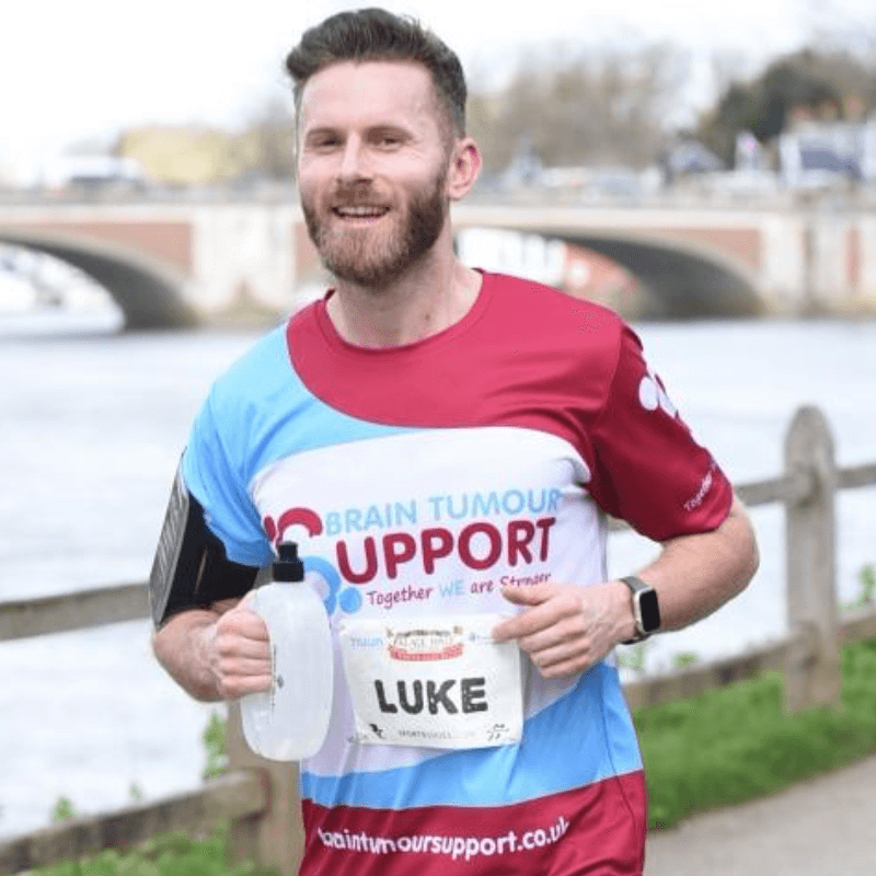 Man running the London Marathon wearing a Brain Tumour Support running shirt and shorts, holding a water bottle