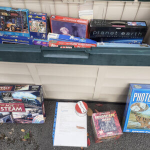 Jigsaw puzzles in and in front of a garden storage box with a small donations tin