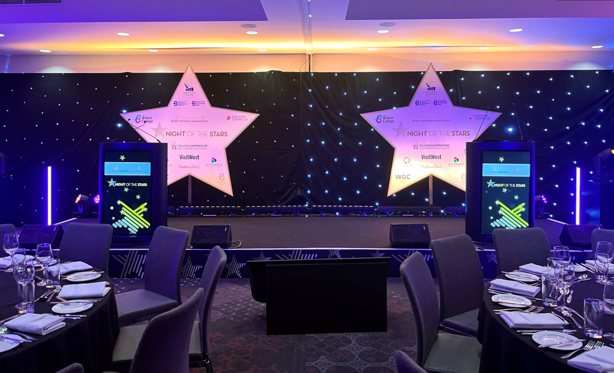 Event stage with two large illuminated stars behind and large round tables set up smartly for dinner