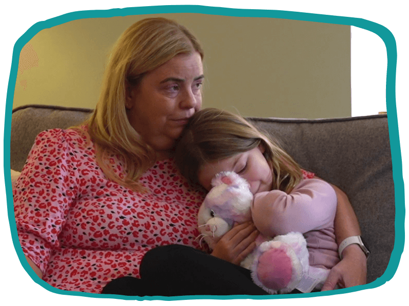 Close-up of Jane sitting on the sofa with her daughter Alice cuddled into her, holding her soft toy.