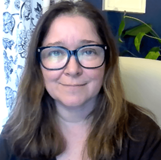 Woman with long brown hair and glasses smiling gently