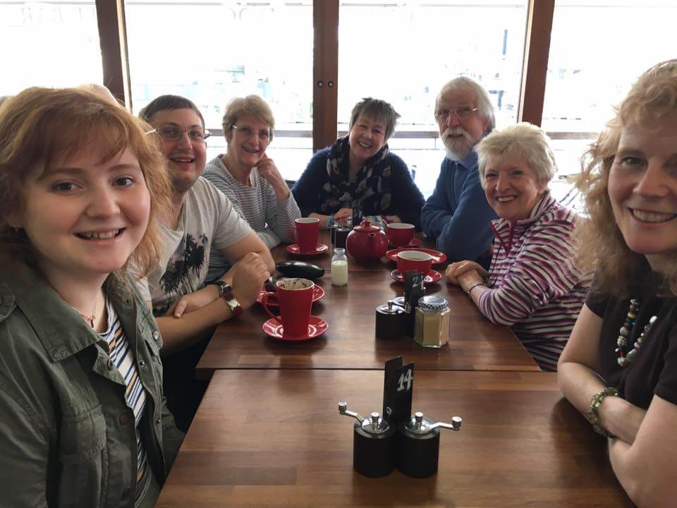Happy smiling group of people sitting around a table with tea and coffee cups in front of them