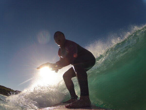 Robert surfing on a wave with the sun shining behind him